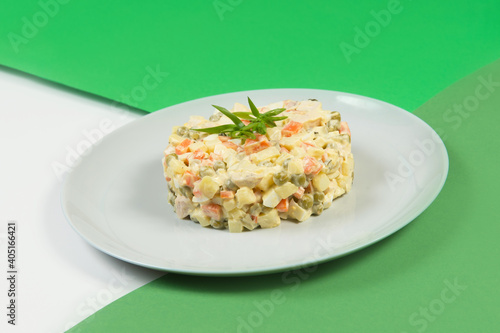 Side view Russian traditional holiday Olivier salad. Dish of boiled vegetables dressed with mayonnaise sauce. Christmas New Year cold dish served on gray plate on green colorful abstract background
 photo