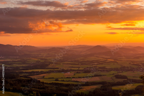 A view of a landscape full of mountains during a golden sunset with the sun on the horizon and a view of the sun from the top of Mount Ondrejnik.