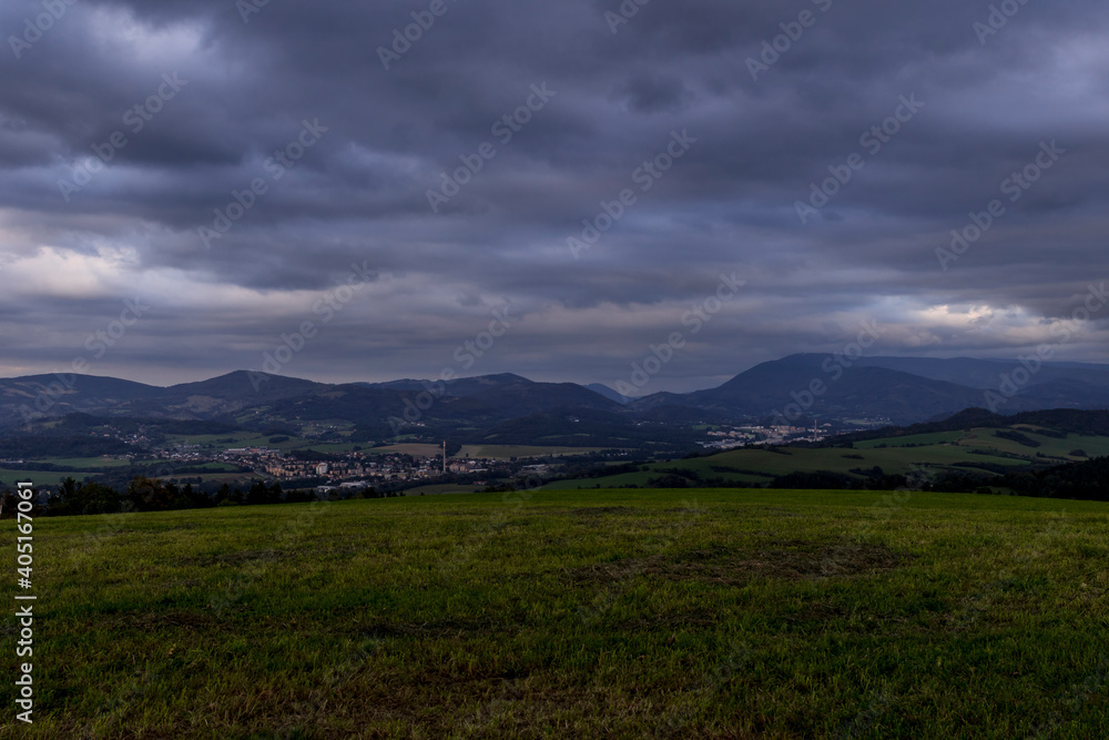 Obraz premium Sunset over mountains and hills with colorful clouds on the horizon that spill from side to side in orange.