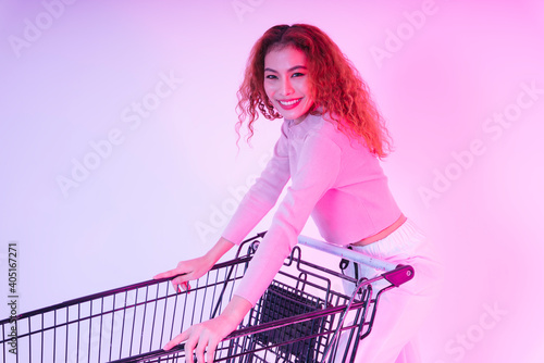 Fashion portrait of asian curly hair in pink shirt with shopping trolley in pink background.