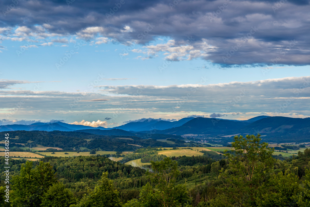 The landscape of the Beskydy Mountains from the viewpoint near Jicin during a colorful sunset and dark clouds in the sky and a view of the surrounding landscape.