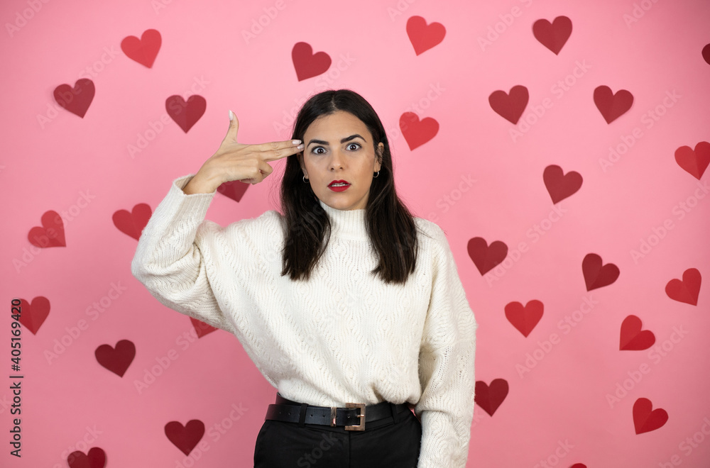 Young beautiful woman over pink background with harts Shooting and killing oneself pointing hand and fingers to head like gun, suicide gesture. Young beautiful woman over pink background with harts Shooting and killing oneself pointing hand and fingers to head like gun, suicide gesture.
