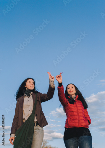 Pair of young caucasian girls sisters in gray and red jackets hold pink paper birds-cranes in their hands against a cloudless blue spring sky. Japanese concept of happiness and good luck.