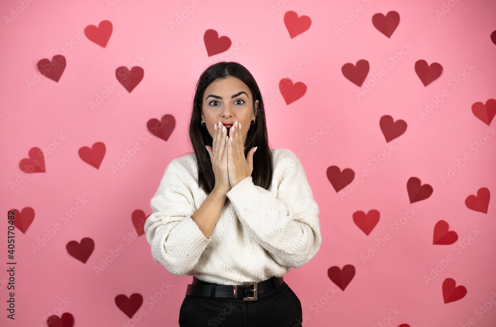 Young beautiful woman over pink background with harts shocked covering mouth with hands for mistake. secret concept. Young beautiful woman over pink background with harts shocked covering mouth with hands for mistake. secret concept.