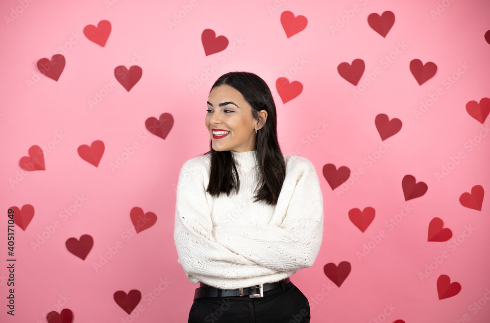 Young beautiful woman over pink background with harts looking to the side with arms crossed convinced and confident Young beautiful woman over pink background with harts looking to the side with arms crossed convinced and confident