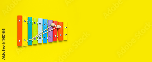 Multicolored wooden xylophone and shock sticks on bright yellow background flat lay top view copy space. Wooden children's musical toy Baby musical instrument Colors of rainbow. Kids natural eco toys