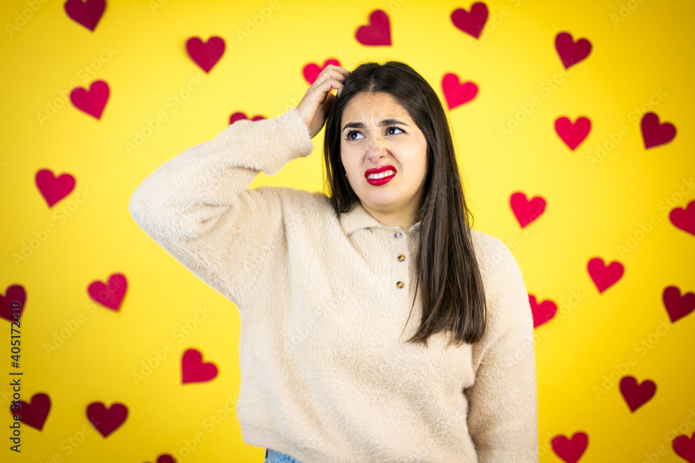 Young caucasian woman over yellow background with red hearts confuse and wonder about question. Uncertain with doubt, thinking with hand on head Young caucasian woman over yellow background with red hearts confuse and wonder about question. Uncertain with doubt, thinking with hand on head