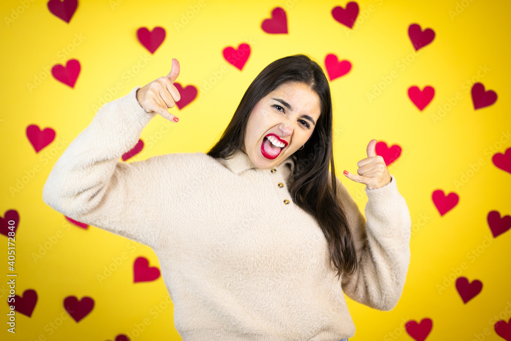 Young caucasian woman over yellow background with red hearts shouting with crazy expression doing rock symbol with hands up Young caucasian woman over yellow background with red hearts shouting with crazy expression doing rock symbol with hands up