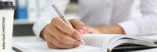 Cropped photo of lady sitting at the table at workplace while making notes in notebook