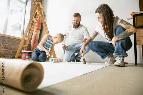 Young couple, family doing apartment repair together themselves. Mother, father and son doing home makeover or renovation. Concept of relations, moving, love. Gluing wallpaper before hanging