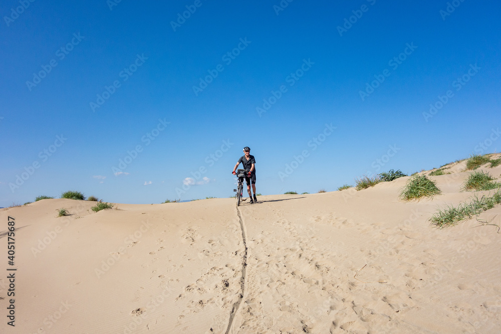 Man walking with bicycle on a sand dune with blue sky, Platja del Fangar,  Spain
