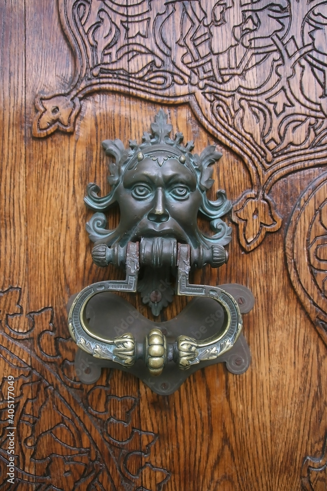 Antique metal door knocker in the form of a  decorative mask on a wooden gate close-up. 