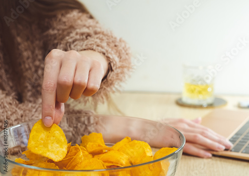 Young woman working at laptop and eating chips