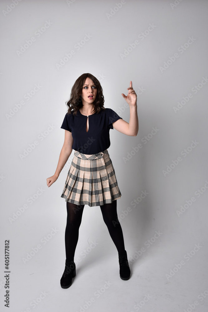 Full length portrait of pretty brunette woman wearing tartan skirt and blouse. Standing pose on the ground, against a studio background. Full length portrait of pretty brunette woman wearing tartan skirt and blouse. Standing pose on the ground, against a studio background.