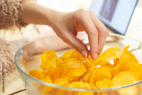 Young woman working at laptop and eating chips