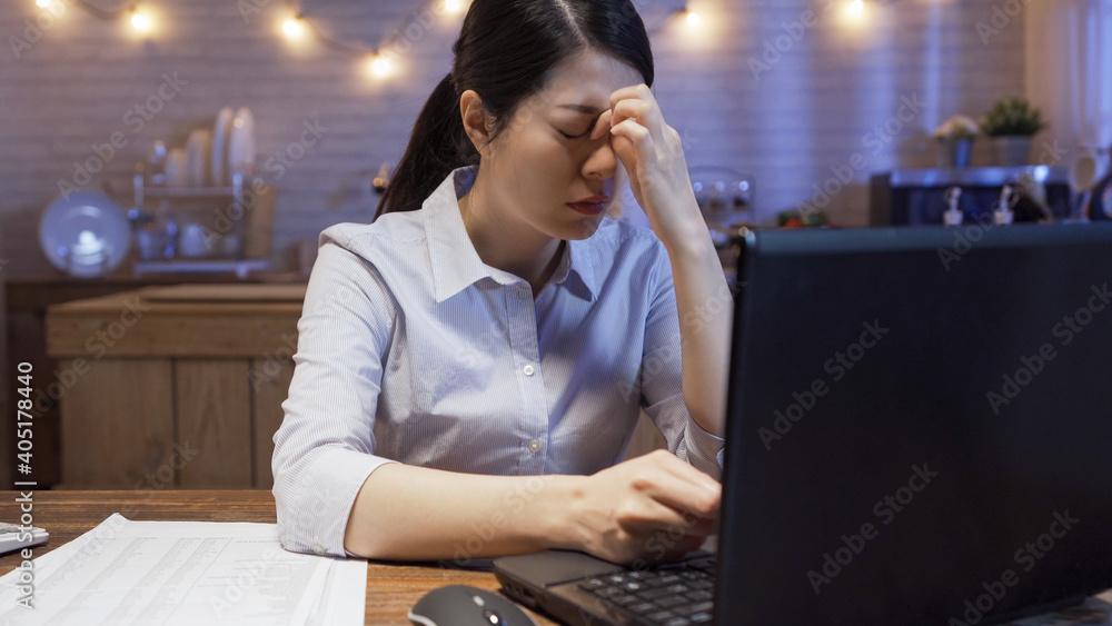 Tired young asian business woman feeling stressed because of deadline project problems. frowning female worker working on laptop computer in kitchen late at night. lady employee with painful eyes. Tired young asian business woman feeling stressed because of deadline project problems. frowning female worker working on laptop computer in kitchen late at night. lady employee with painful eyes.