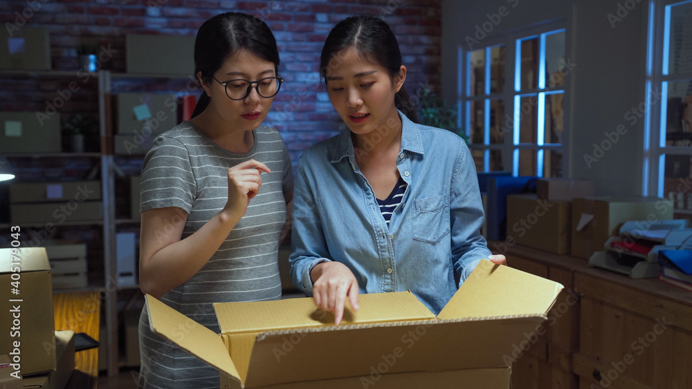Two Asian businesswoman team success have new order from customer after Start up small business entrepreneur together. young girl staffs discussing with cardboard box at dark workplace at night. Two Asian businesswoman team success have new order from customer after Start up small business entrepreneur together. young girl staffs discussing with cardboard box at dark workplace at night.