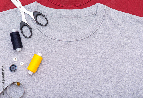 Simply composition with buttons, tape measure, scissors, spool of thread. Sewing equipment on gray t-shirt, lay out, top view.