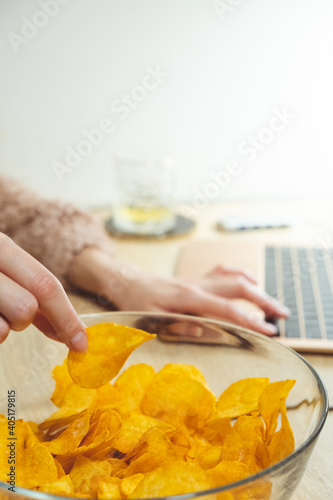 Young woman working at laptop and eating chips