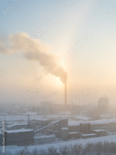 The chimney of a steaming power plant emerges from the back fog. The chimney of the power plant rises above the surrounding fog. Energy. Heating plant in operation. photo