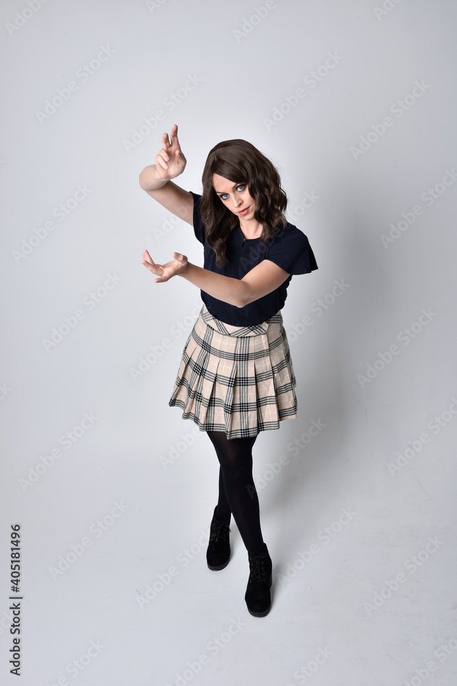 Full length portrait of pretty brunette woman wearing tartan skirt and blouse. Standing pose on the ground, against a studio background. Full length portrait of pretty brunette woman wearing tartan skirt and blouse. Standing pose on the ground, against a studio background.