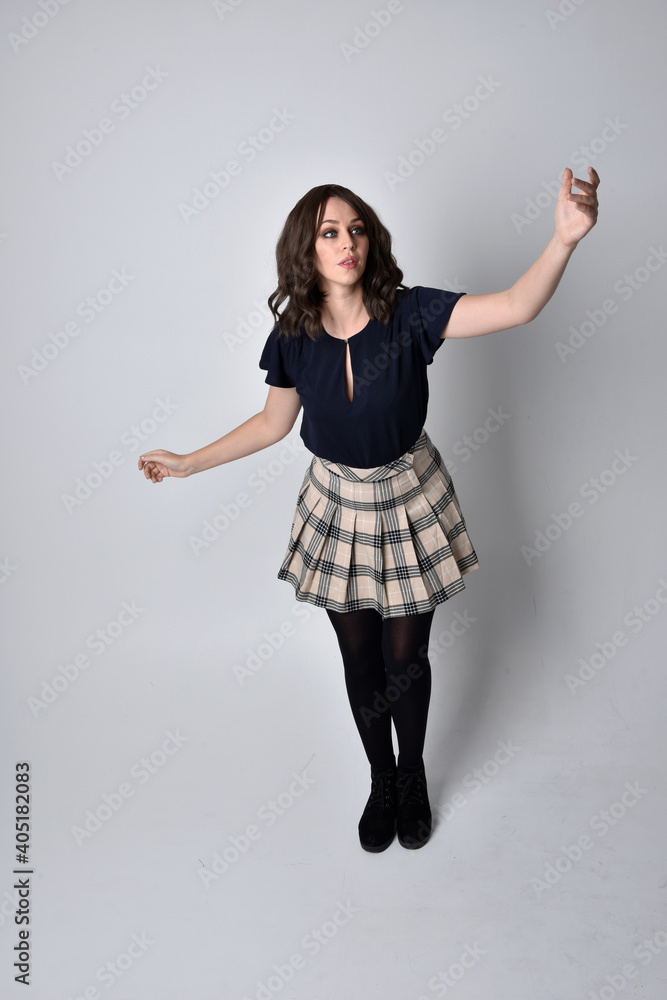 Full length portrait of pretty brunette woman wearing tartan skirt and blouse. Standing pose on the ground, against a studio background. Full length portrait of pretty brunette woman wearing tartan skirt and blouse. Standing pose on the ground, against a studio background.
