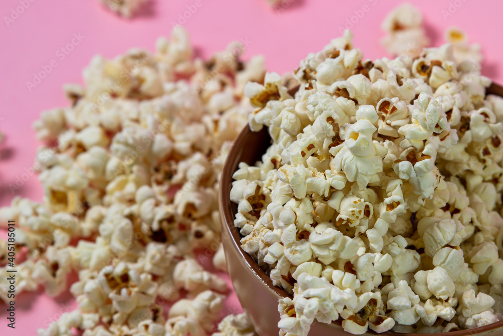 Popcorn on a pink background. A full plate of popcorn. Popcorn is scattered around. Movie snack Popcorn on a pink background. A full plate of popcorn. Popcorn is scattered around. Movie snack