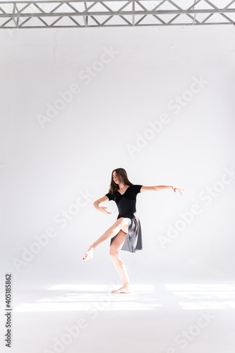 A slender girl in a black sports dress poses while dancing on a white isolated background. Girl athlete dancing on a white isolated background with place for text or logo.