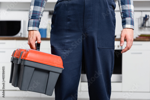 cropped view of young repairman holding toolbox with blurred kitchen on background