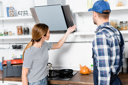 Fototapeta Naklejka Na Ścianę i Meble -  young woman pointing with hand at shelves near handyman in kitchen