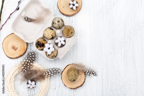 Easter quail eggs, nest and cotton flowers on white wooden background. Top view, copy space.