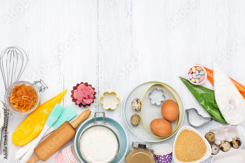 Cooking Easter background with rolling pin, eggs, whisk for whipping, cookie cutters, sugar sprinkling, flour. Rustic white wooden background, top view copy space.