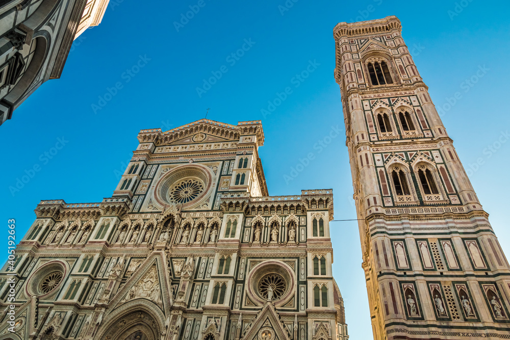 Great low-angle view of the beautiful marble facade of the famous Florence Cathedral Santa Maria del Fiore with the free-standing Giotto's Campanile in the Piazza del Duomo on a sunny day with a blue.