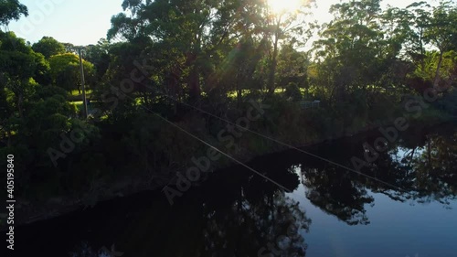 Slow aerial rise over river and trees facing the sun at sunrise in Australian outback photo