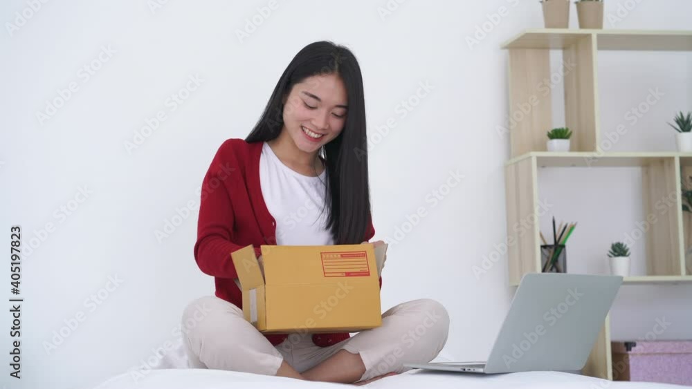 Happy amazed young asian girl consumer holding opening cardboard box sit on bed at home Happy amazed young asian girl consumer holding opening cardboard box sit on bed at home