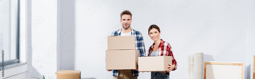 smiling young couple with boxes looking at camera indoors, banner smiling young couple with boxes looking at camera indoors, banner