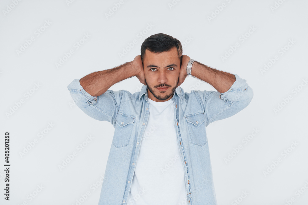 Covers his ears. Young handsome man standing indoors against white background Covers his ears. Young handsome man standing indoors against white background