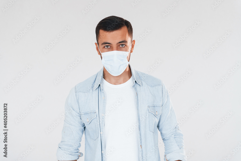 In protective mask. Young handsome man standing indoors against white background In protective mask. Young handsome man standing indoors against white background