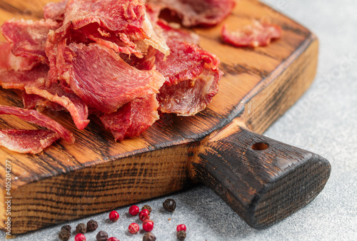 Meat chips. Pork or beef meat chip slices on a wooden board on a gray concrete background. Selective focus, copy space,