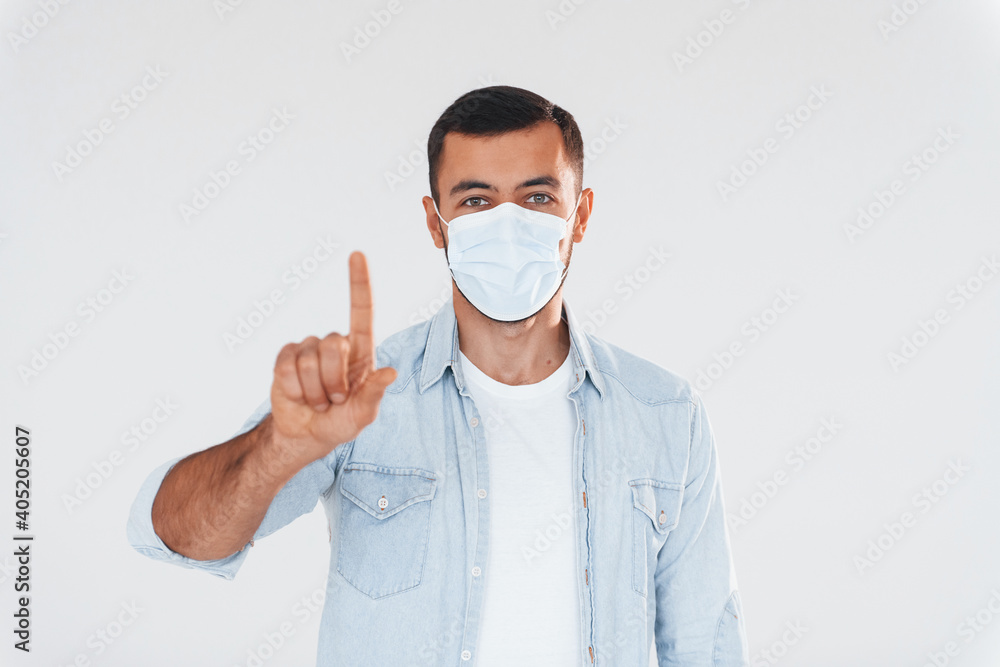 In protective mask. Young handsome man standing indoors against white background