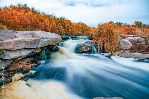 Stream runs among white wet stones covered with grass in golden autumn
