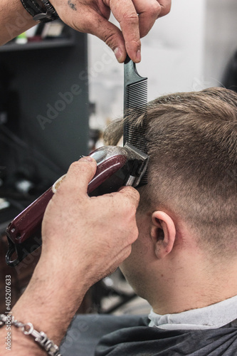 a barber in a barbershop cuts a man's hair. hands holding an electric hair clipper. professional haircut at home during quarantine and pandemic