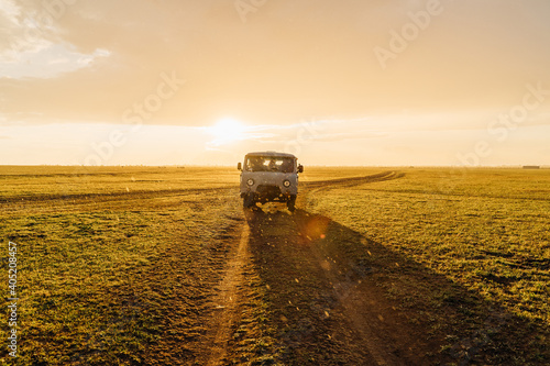 Adventure spirit. Old post soviet off-road vehicle car UAZ bus rides on a country road.  Warm beautiful Sunset sepia light and  raining. Backlight. romantic nostalgic movie cinematic horizontal photo