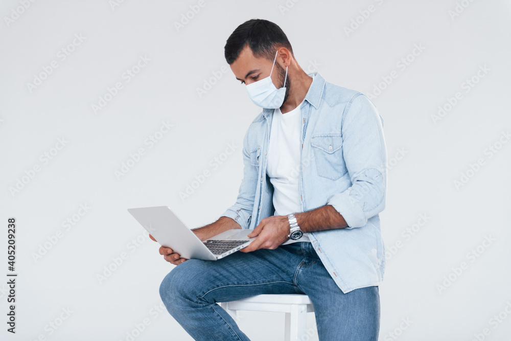 Uses laptop. Young handsome man standing indoors against white background Uses laptop. Young handsome man standing indoors against white background