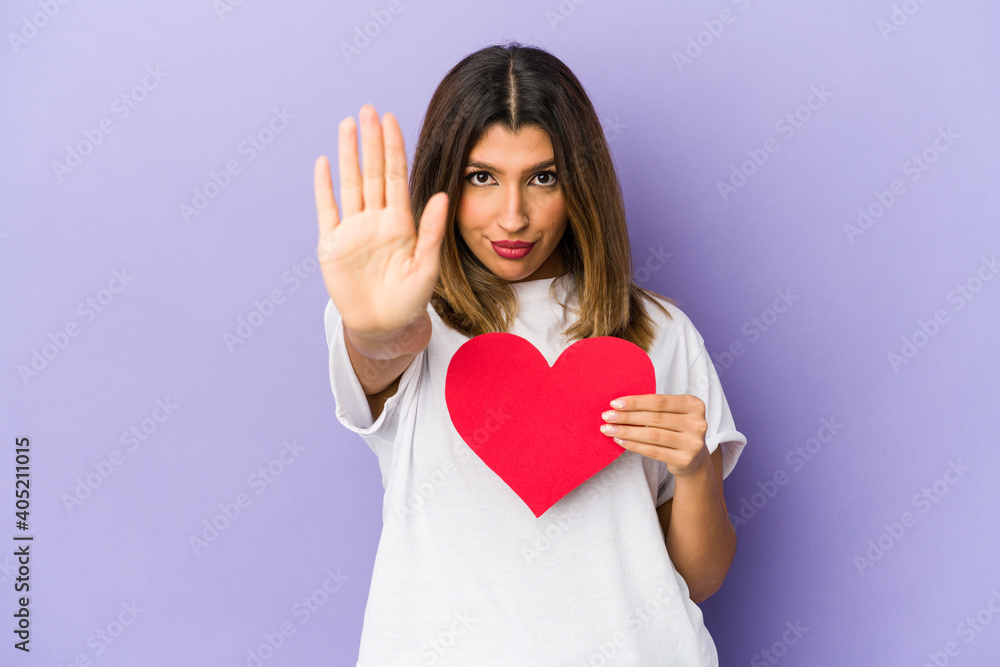 Young indian woman holding a valentines day heart isolated standing with outstretched hand showing stop sign, preventing you. Young indian woman holding a valentines day heart isolated standing with outstretched hand showing stop sign, preventing you.