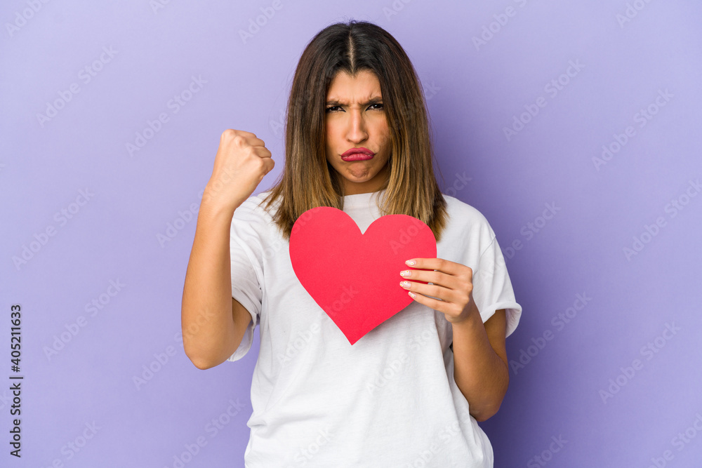 Young indian woman holding a valentines day heart isolated showing fist to camera, aggressive facial expression. Young indian woman holding a valentines day heart isolated showing fist to camera, aggressive facial expression.