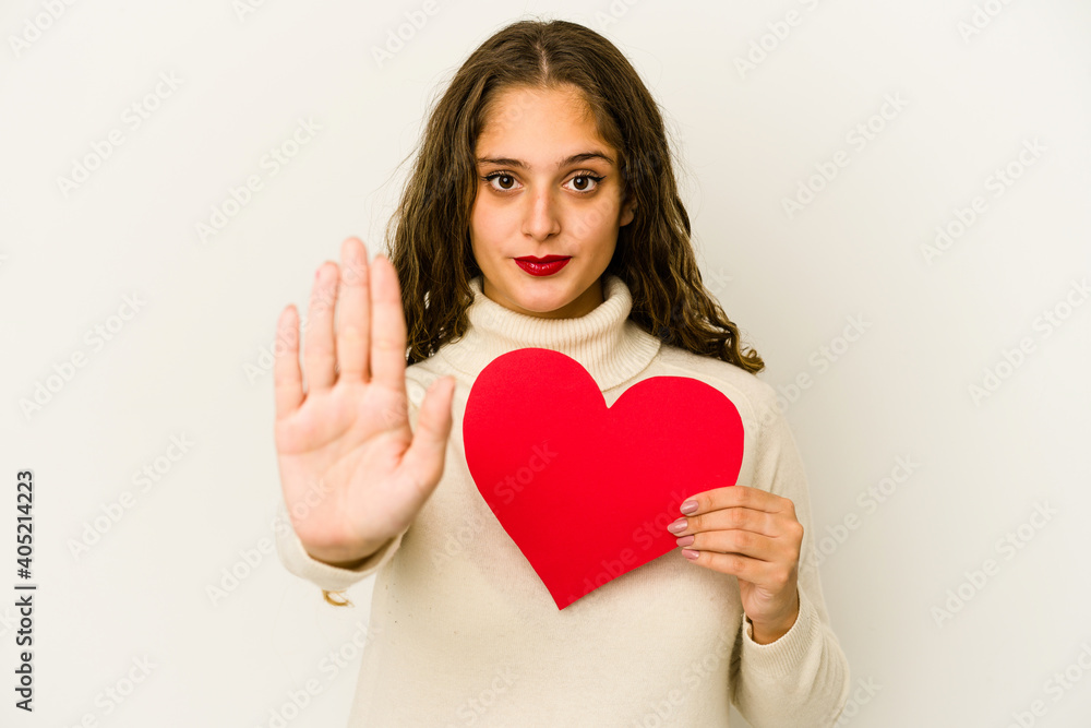 Young caucasian woman holding a heart valentines day shape isolated standing with outstretched hand showing stop sign, preventing you. Young caucasian woman holding a heart valentines day shape isolated standing with outstretched hand showing stop sign, preventing you.