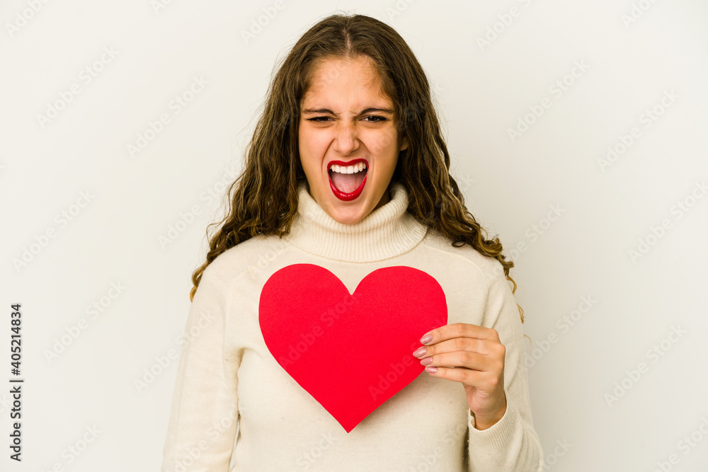 Young caucasian woman holding a heart valentines day shape isolated screaming very angry and aggressive. Young caucasian woman holding a heart valentines day shape isolated screaming very angry and aggressive.