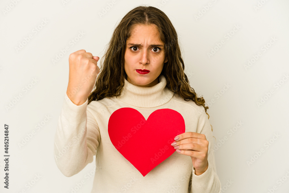 Young caucasian woman holding a heart valentines day shape isolated showing fist to camera, aggressive facial expression. Young caucasian woman holding a heart valentines day shape isolated showing fist to camera, aggressive facial expression.
