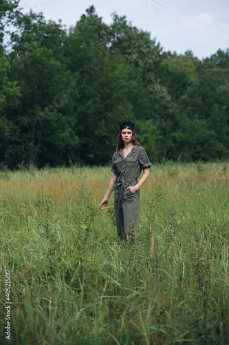 Woman in the meadow Against the background of green trees in a green overalls 